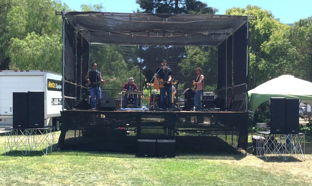 Band playing on an outdoor festival stage with speakers on each side